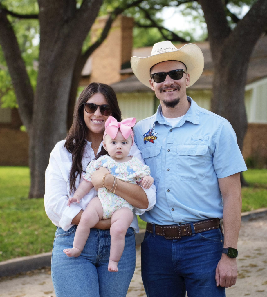 Family Photo of husband and wife standing side by side with wife holding baby girl